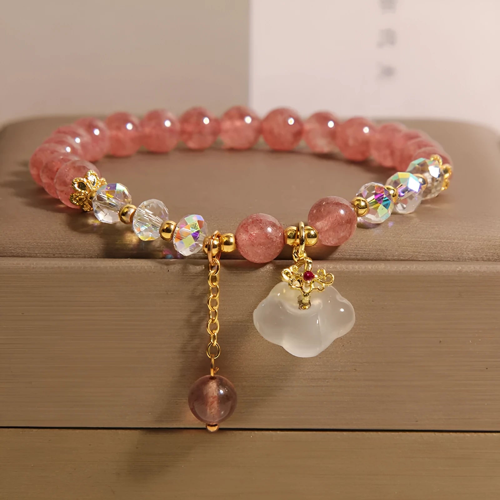 Women's natural strawberry quartz and white agate crystal bracelet with auspicious cloud pattern on a flat surface