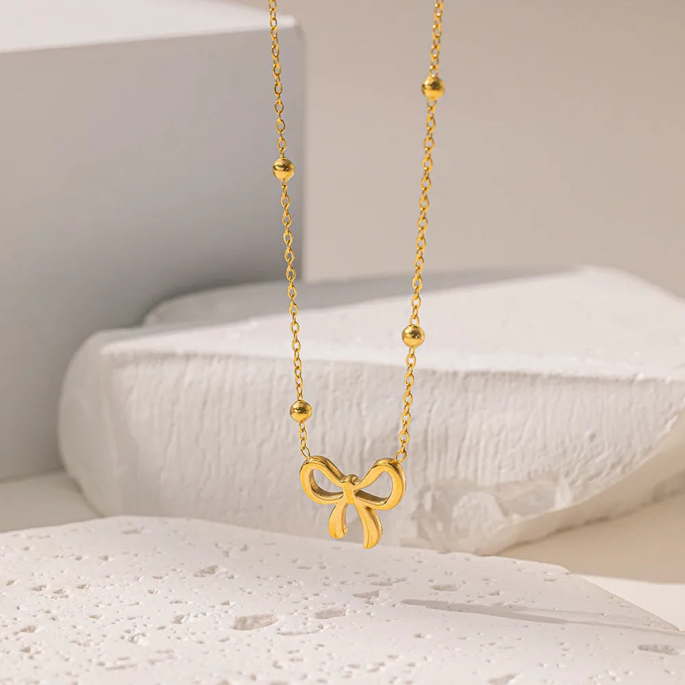 Gold titanium steel bow necklace with cross chain design on display