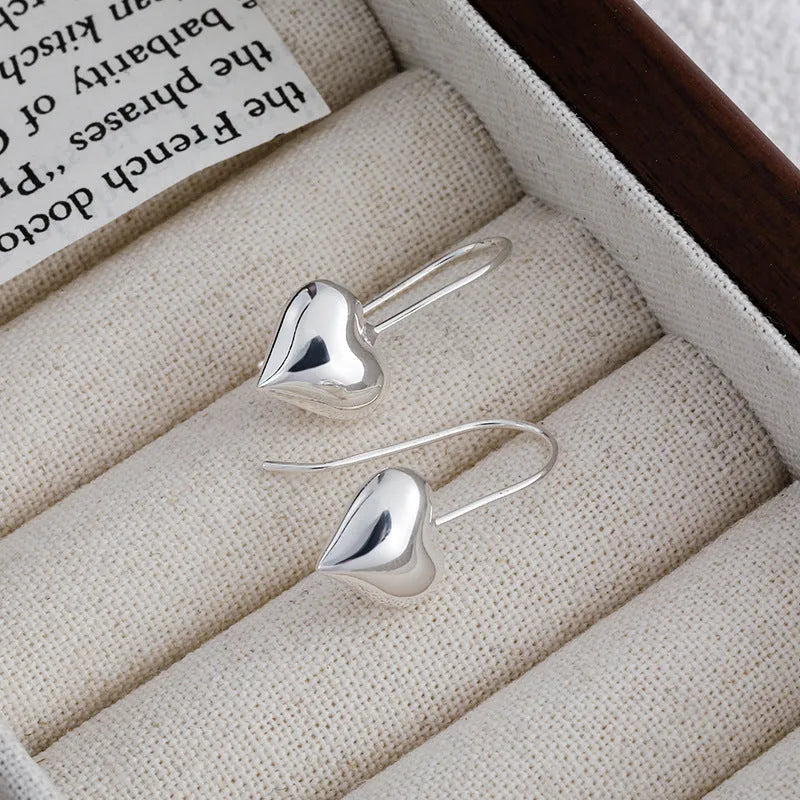 Close-up of glossy silver three-dimensional heart-shaped earrings on a white background.