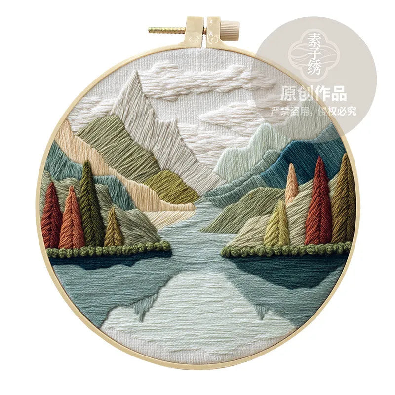 Embroidery DIY kit with cotton landscape fabric, bamboo frame, threads, and tools on wooden surface
