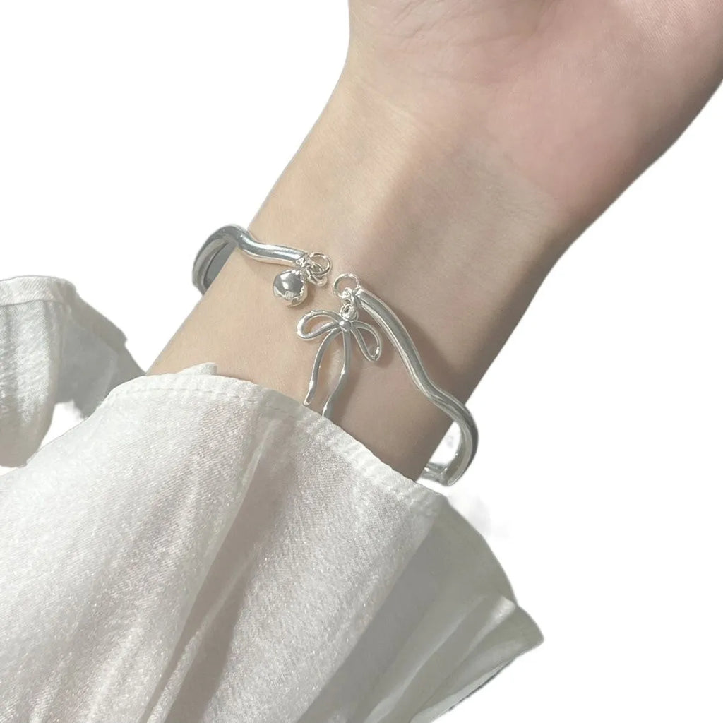 Silver adjustable bracelet with bow charm and small bell detail on wrist