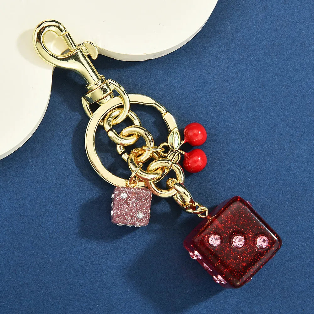 Close-up of a square metal keychain pendant with a vintage cherry two-tone dice pattern.