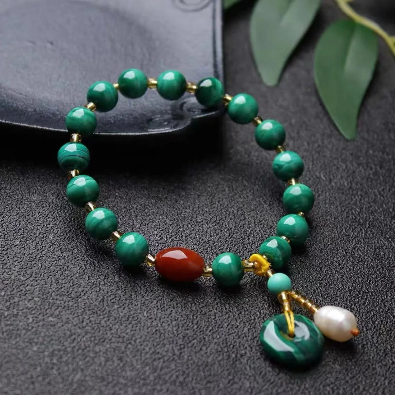 Handmade natural malachite and red agate barrel bead bracelet on a wrist, showing green and red stone details.