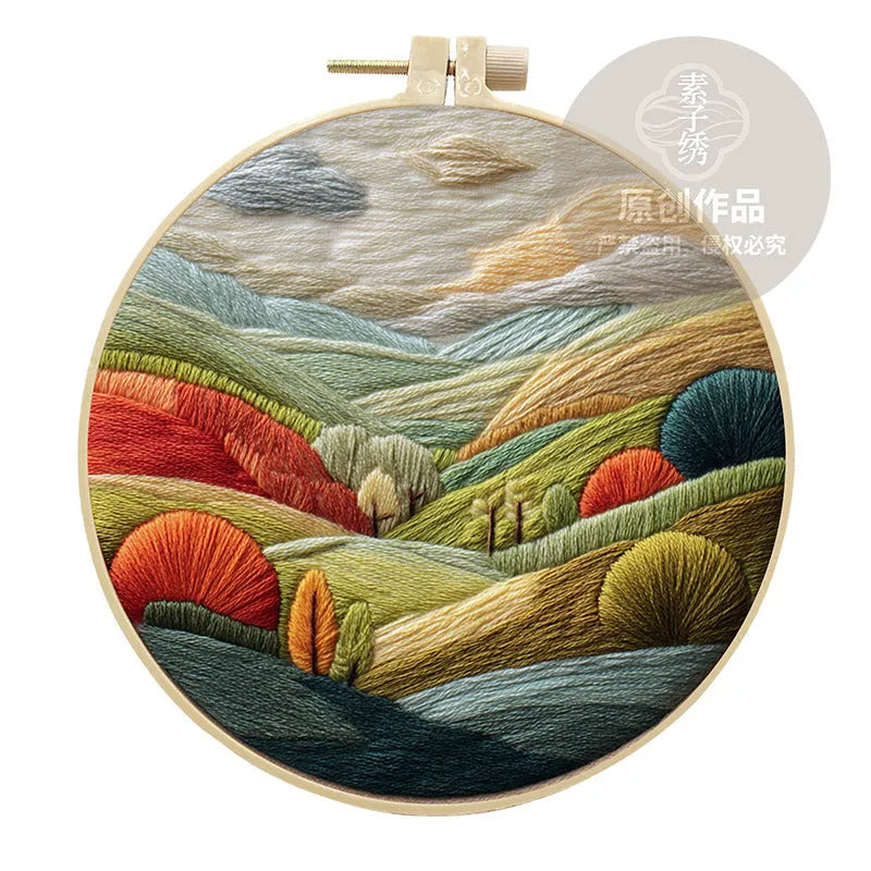Embroidery DIY kit with cotton landscape fabric, bamboo frame, threads, and tools on wooden surface