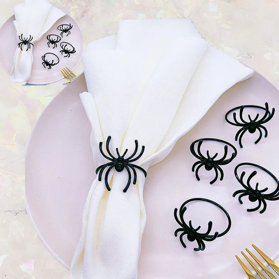 Six black alloy spider-shaped napkin rings for Halloween table decoration on a dark surface.